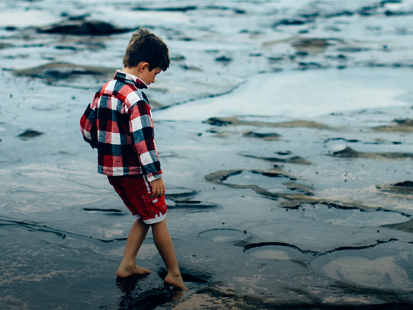 Boy standing testing the water from a rock